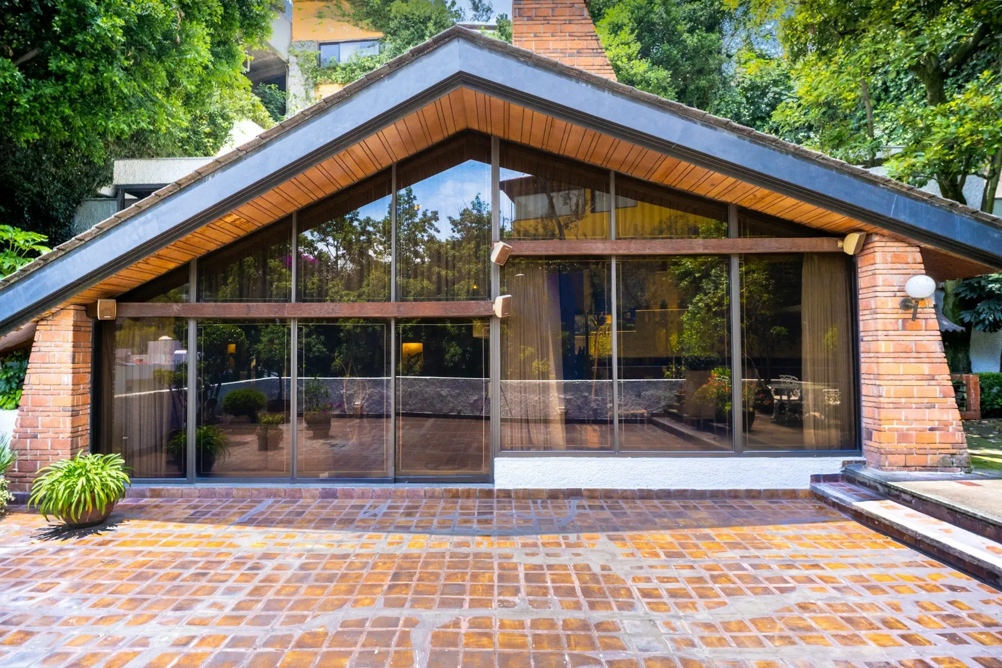 Gabled house with a timber-lined soffit over a full-height glass wall and a brick terrace