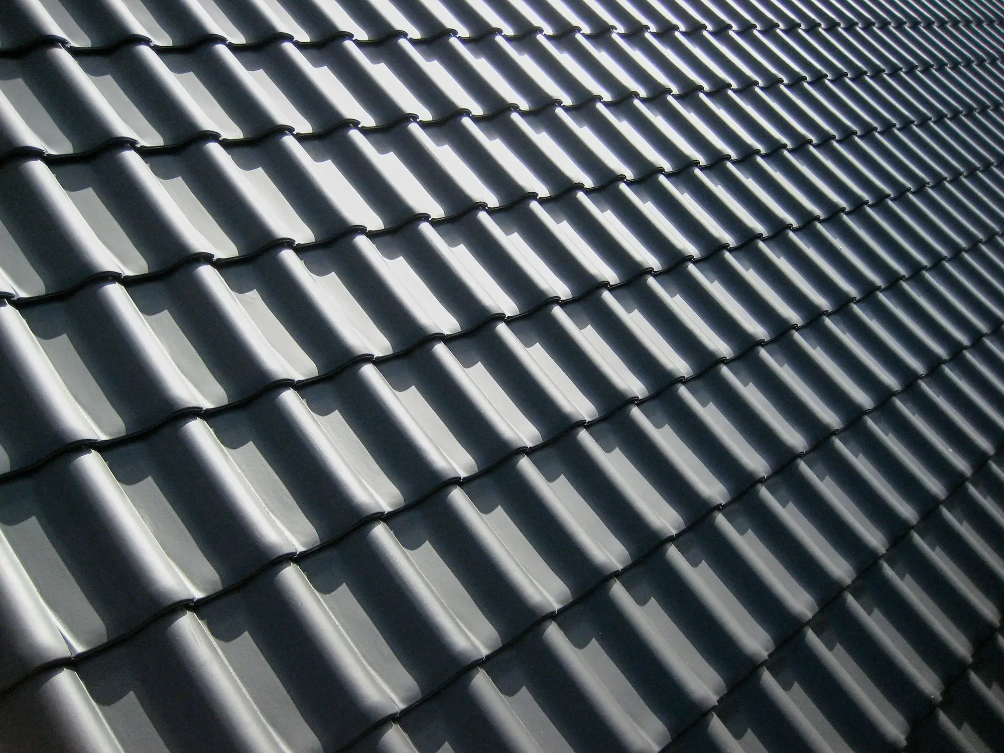 Rows of dark grey roof tiles casting sharp shadows in bright light