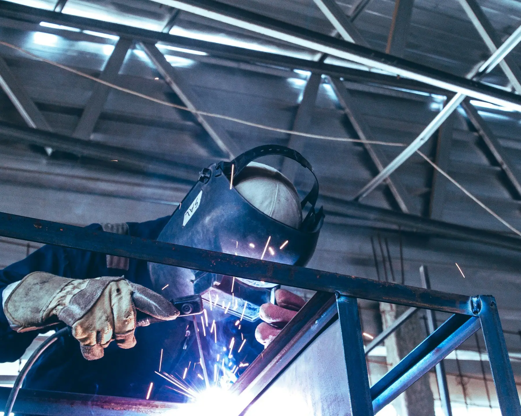 Welder in a mask joining a steel frame, sparks flying