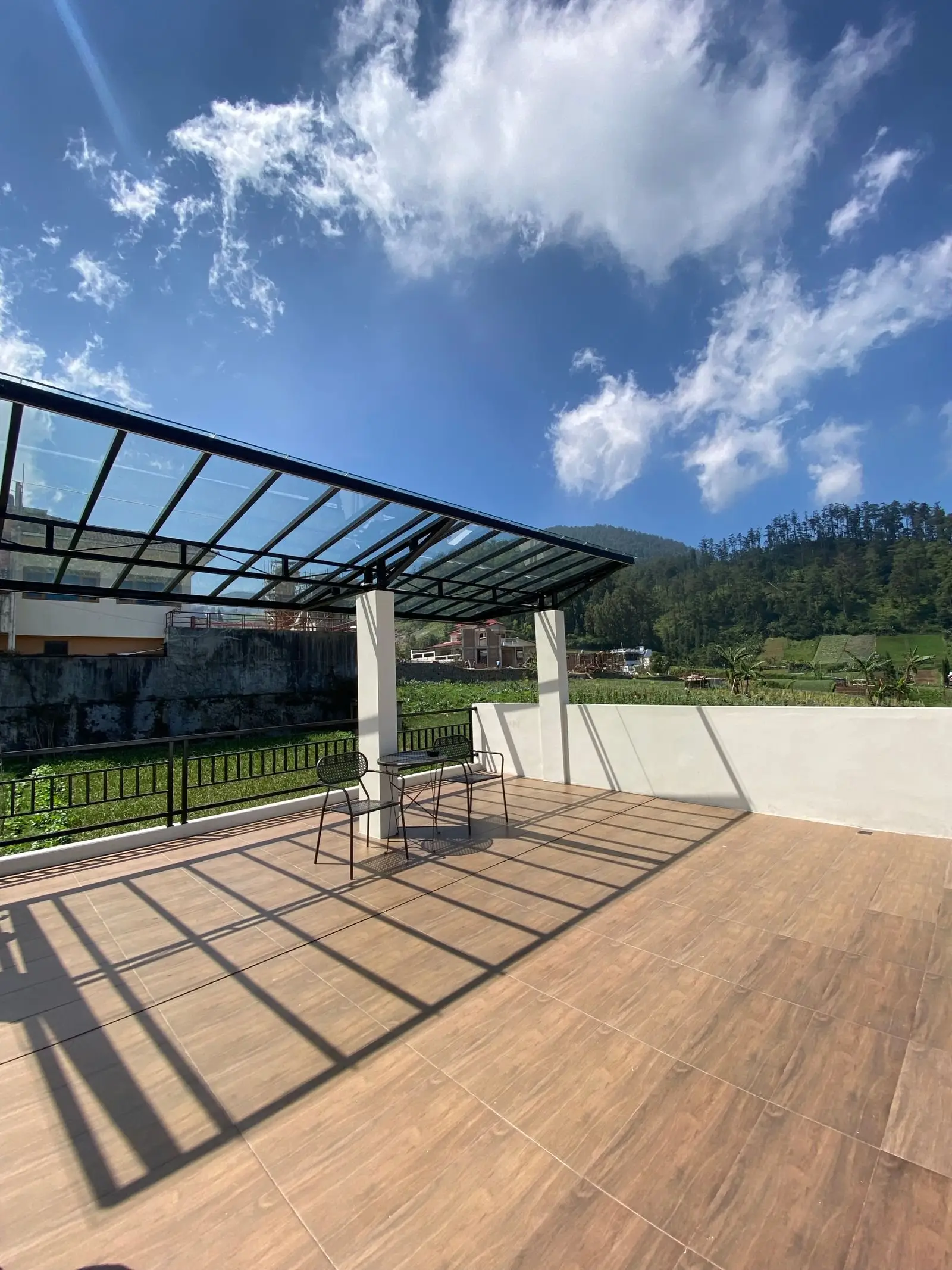 Glass canopy on a dark steel frame over a timber-decked terrace with hill views
