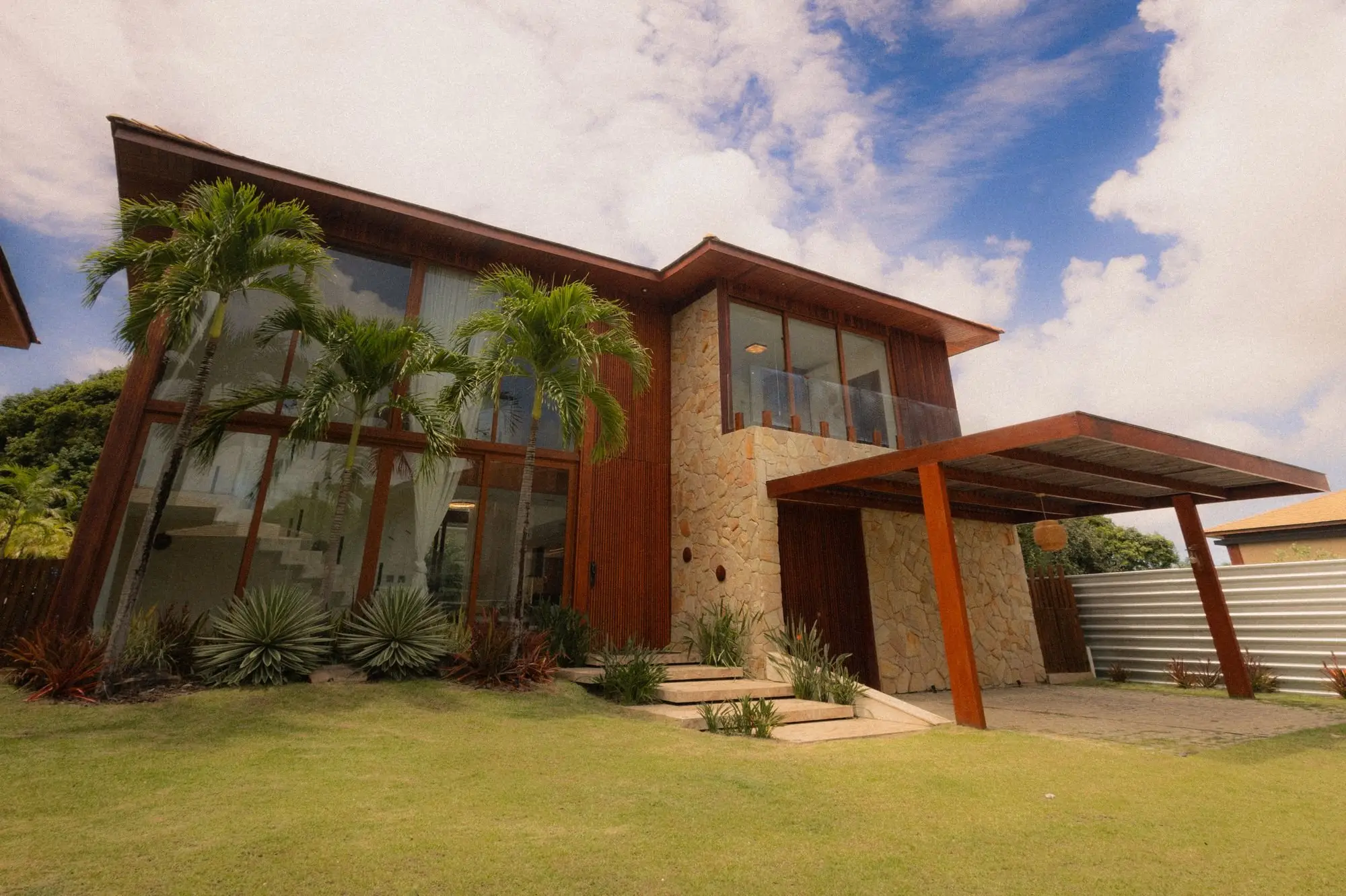Modern tropical home with stone and timber walls, tall glass windows and a steel-framed porch canopy